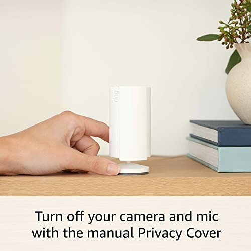 Hand adjusting a smart camera with a privacy cover on a table.